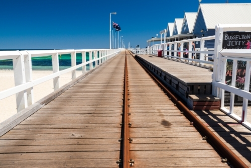 A long  Jetty with train lines leading to a distant horizon with a clear blue sky - Australian Stock Image