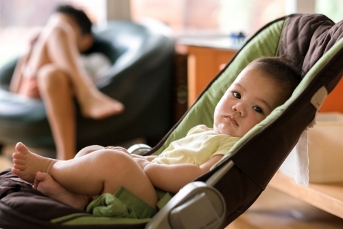 A lounging baby looking relaxed, while his big brother is watching TV on the background - Australian Stock Image