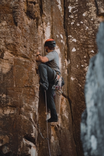 A male rock climber placing 'trad' gear into a cliff for a climbing route at Diamond Beach. - Australian Stock Image