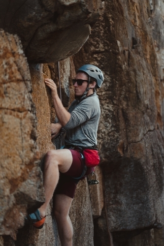 A male rock climber tackling a climbing route at Diamond Beach. - Australian Stock Image