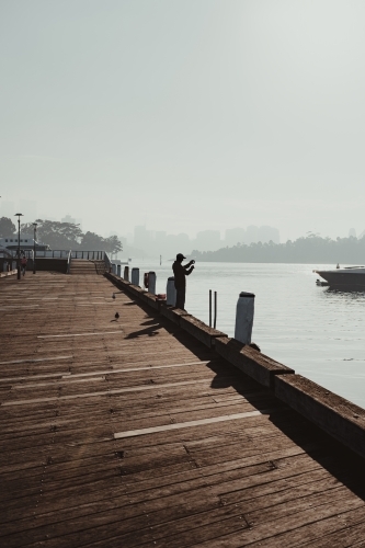 A man fishing on a hazy morning beside the water at Pirrama Park/Jones Bay Wharf. - Australian Stock Image