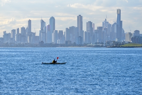 A man paddles an ocean kayak on  Port Phillip Bay with the Melbourne city skyline in the background - Australian Stock Image