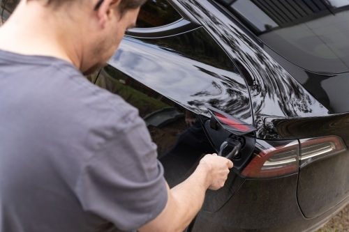 A man plugging in an electric Ev vehicle car to a home charger station plug - Australian Stock Image