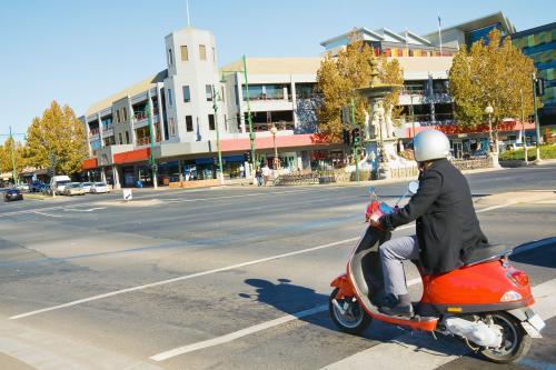 A man riding a scooter through an city intersection - Australian Stock Image