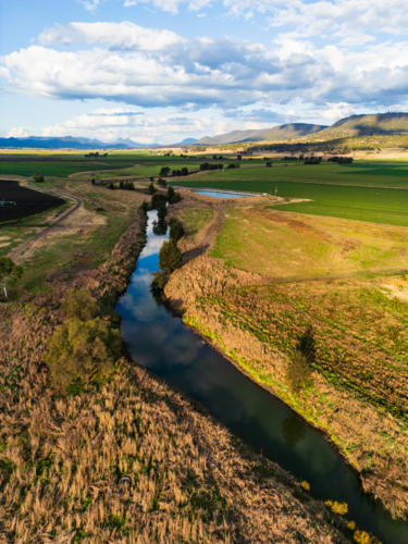 A meandering creek  with water surrounded by agricultural fields - Australian Stock Image