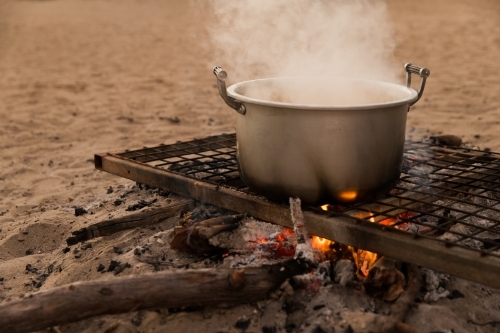 A metal pot on a grill over an open fire. - Australian Stock Image