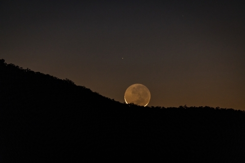 A new moon rising over a mountain ridge - Australian Stock Image