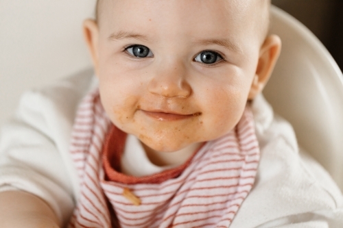 A one year old baby with blue eyes, she has a dirty face as she has been feeding herself spaghetti - Australian Stock Image