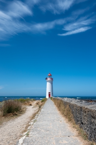 A pathway leading to a white lighthouse with a red top - Australian Stock Image