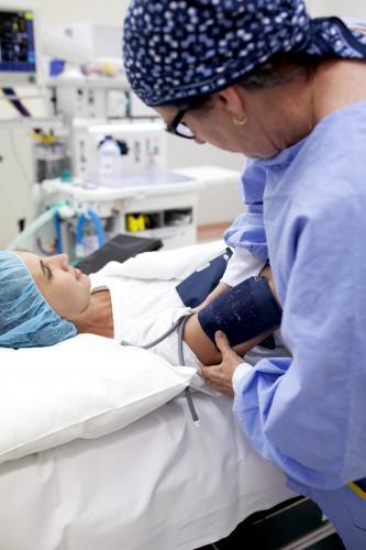 A patient lying on a bed in a hospital operating theatre with nurse taking blood pressure - Australian Stock Image