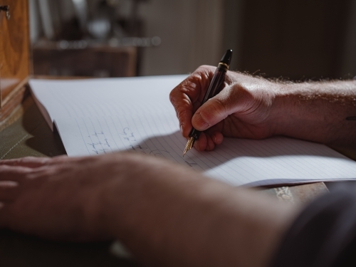 A person's hand holding a pen and writing on a lined notebook - Australian Stock Image