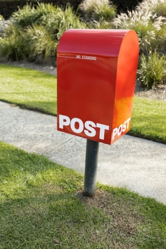 A red Australia post letter box beside footpath - Australian Stock Image