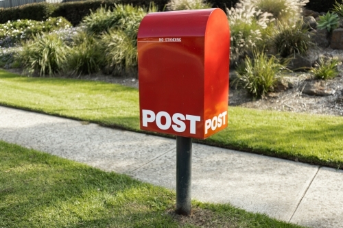 A red Australia post letter box beside footpath - Australian Stock Image