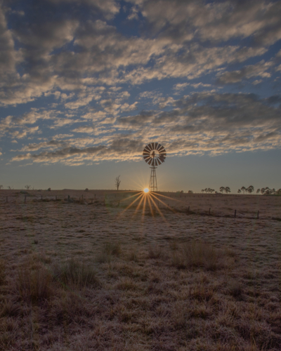 A rising sun, a country windmill and a cloudy sky - Australian Stock Image