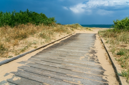 A sandy coastal boardwalk leading towards a dark sky - Australian Stock Image