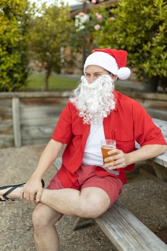 A Santa Claus at Christmas time in  the Australian summer holding a beer - Australian Stock Image