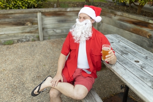 A Santa Claus at Christmas time in  the Australian summer holding a beer - Australian Stock Image