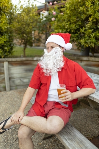 A Santa Claus at Christmas time in  the Australian summer holding a beer - Australian Stock Image