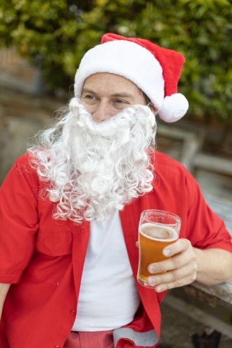 A Santa Claus at Christmas time in  the Australian summer holding a beer - Australian Stock Image