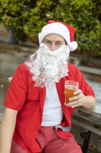 A Santa Claus at Christmas time in  the Australian summer holding a beer - Australian Stock Image