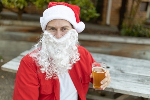 A Santa Claus at Christmas time in  the Australian summer holding a beer - Australian Stock Image