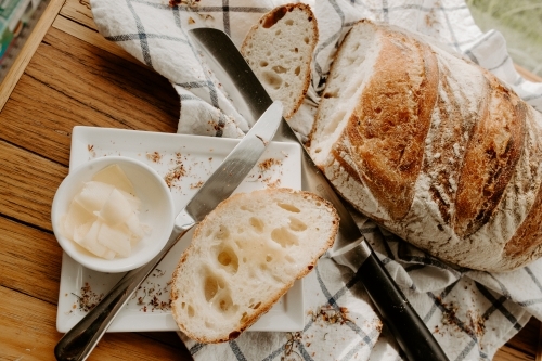A slice of bread on a white plate with butter with Home made Sour dough bread cooling on a tea towel - Australian Stock Image