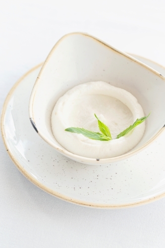 A small bowl of garlic dip topped with herb. - Australian Stock Image