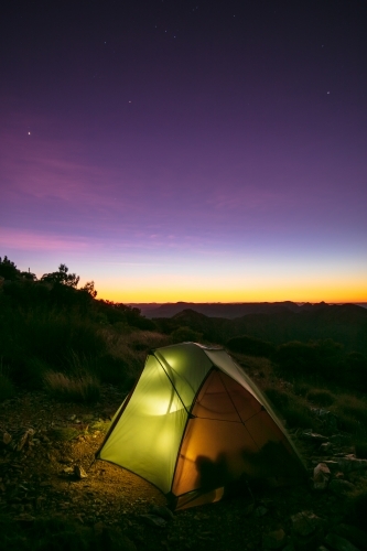A small two person tent illuminated from a camper inside the tent at night. - Australian Stock Image