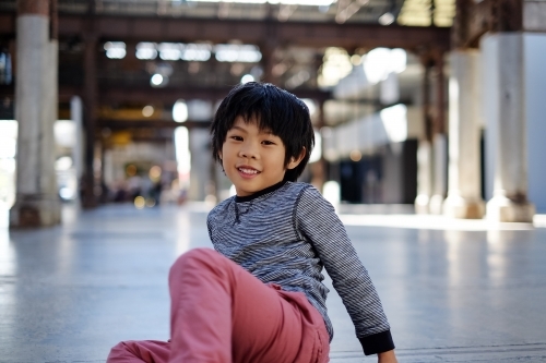 a smiling happy kid sitting on an empty industrial space - Australian Stock Image