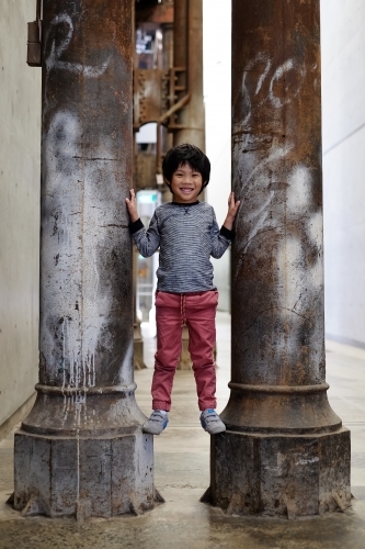 a smiling happy kid standing between two pillars - Australian Stock Image