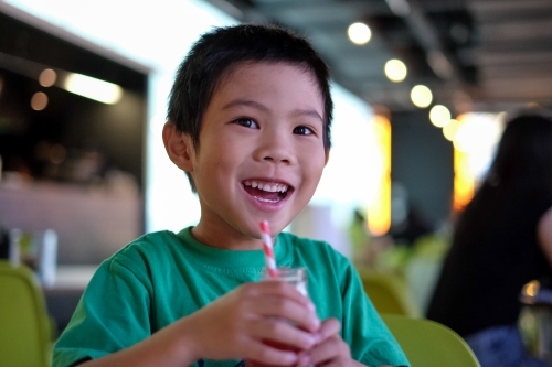 a smiling kid, enjoying a drink at a cafe - Australian Stock Image