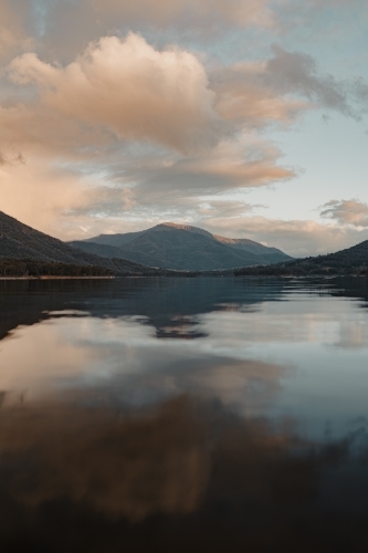 A smooth, still lake with mountains in the background at sunset - Australian Stock Image