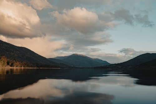 A smooth, still lake with mountains in the background at sunset - Australian Stock Image