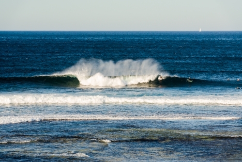 A spectacular wave in a blue ocean with surfers lit by the early morning light - Australian Stock Image