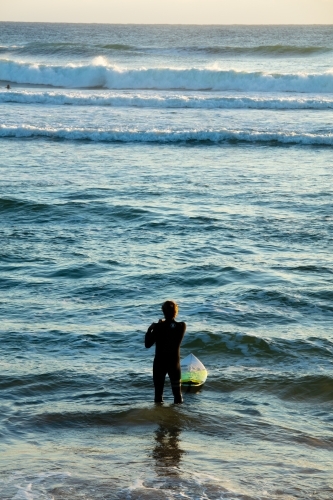 A surfer stands in the water adjusting his wetsuit before going for a surf at Cabarita. - Australian Stock Image