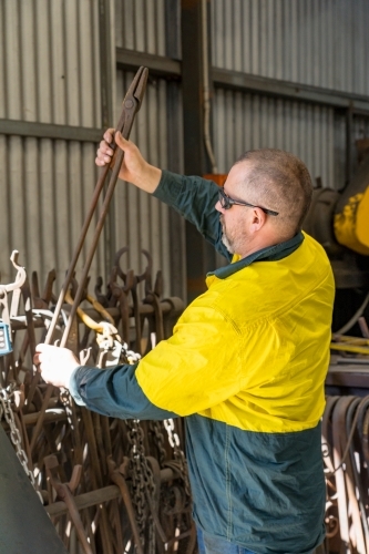 A tradesman wearing high vis clothing lifting a pair of long steel tongs - Australian Stock Image