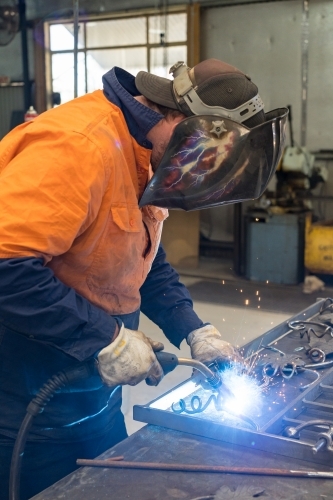 A tradesman wearing high vis clothing welding steel on a workbench - Australian Stock Image