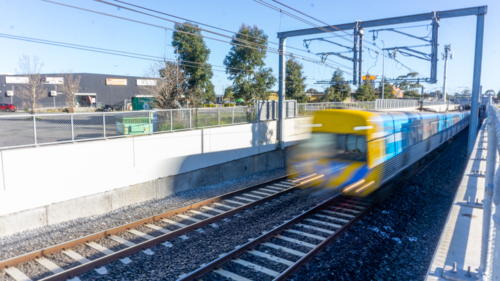 A train moving through a shallow cutting under overhead wires - Australian Stock Image