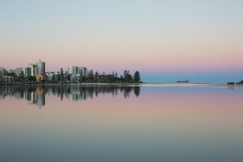 A tranquil waterfront cityscape at twilight, with pastel sky and a reflection of buildings in water - Australian Stock Image