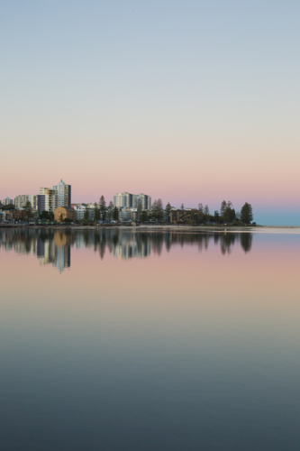 A tranquil waterfront cityscape at twilight, with pastel sky and a reflection of buildings in water - Australian Stock Image