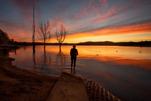 A traveller watching the beautiful colourful sky and reflections on Lake Jindabyne - Australian Stock Image