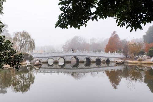 A white, multi-arched bridge crossing over a calm water. - Australian Stock Image