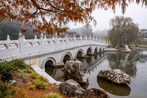 A white, multi-arched bridge crossing over a calm water. - Australian Stock Image