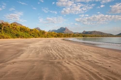 A wide, long beach with mountains in the background taken at dawn - Australian Stock Image