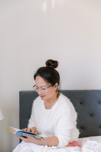 A woman reading books in her bedroom - Australian Stock Image