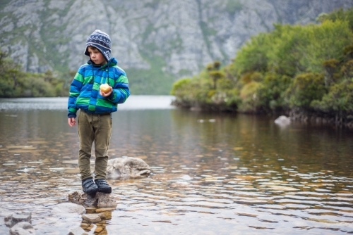 A young boy standing on a rock in a river - Australian Stock Image