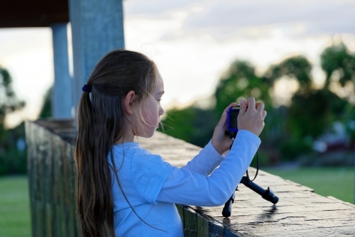A young girl holding a camera on a tripod learning to photograph - Australian Stock Image