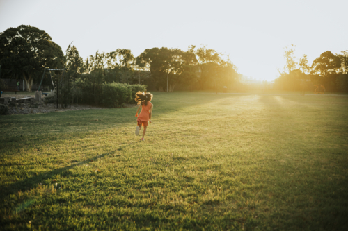 A young girl running at the park towards sunset - Australian Stock Image