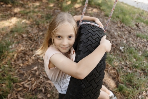 A young girl sitting in a tyre swing outdoors - Australian Stock Image
