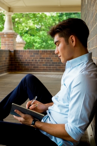 A young male sitting on the ground on a covered verandah - Australian Stock Image